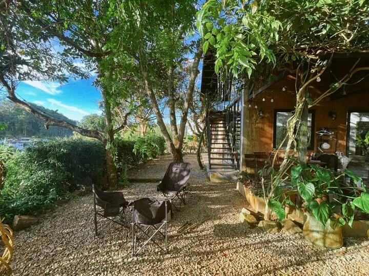 Folding chairs in a tree-shaded gravel garden beside the house and exterior stairs.