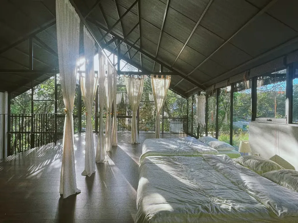 Sunlight reaches the curtained mezzanine beds beside the glass wall.