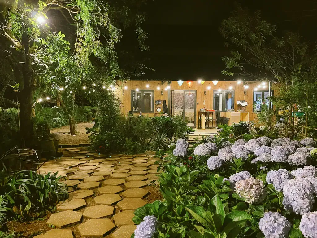 House lit after dark behind a garden path and flowering hydrangeas.