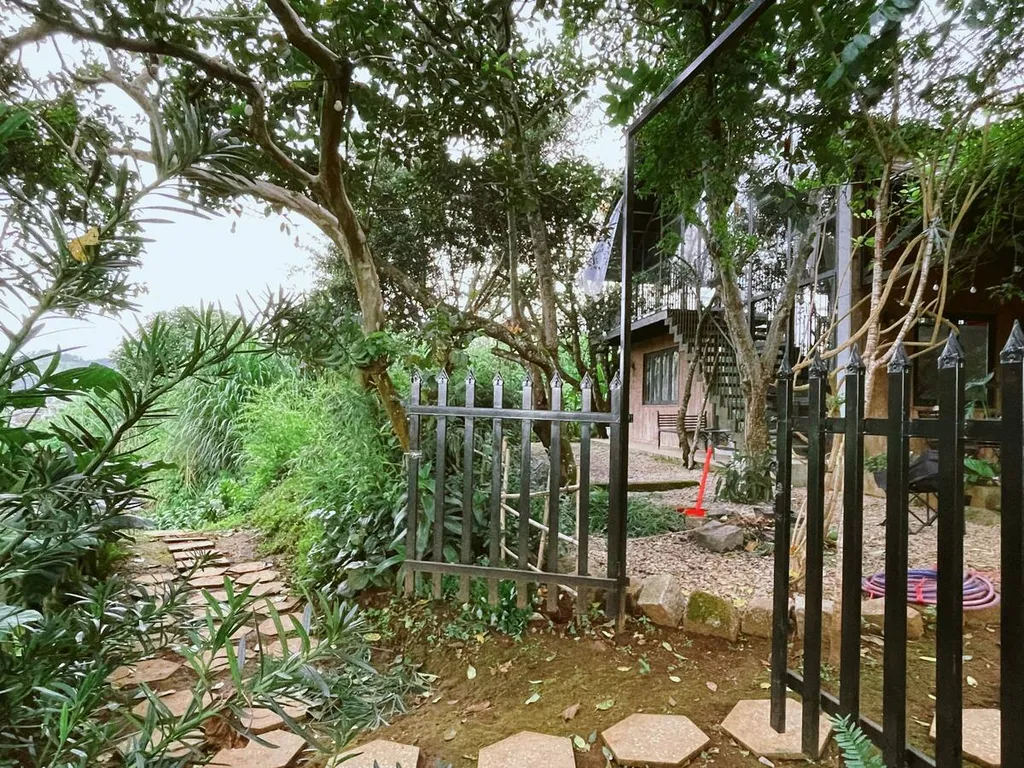 Open garden gate framed by trees and flowering plants.